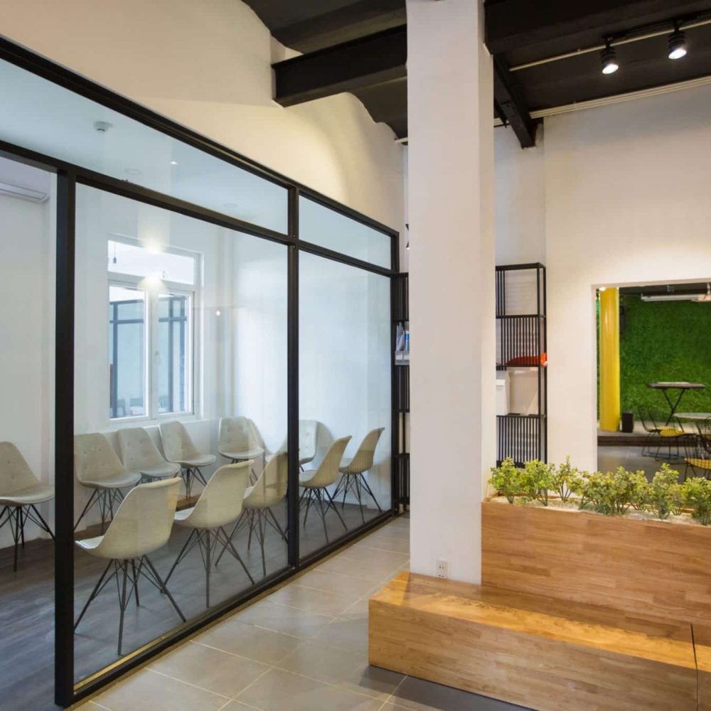 Nobody in office lobby with wooden bench. White wall with column and shelves. Green plants as part of interior. Many chairs behind glassy wall. Business center concept